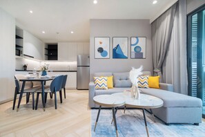 Ein modernes Wohnzimmer mit grauem Sofa, einem Esstisch mit Stühlen und einer Küche im Hintergrund.