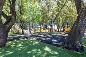 A playground with swings and a slide, surrounded by trees and grass. - Apartment 'Casa Orizzonte Anglona' with Private Terrace, Garden and Wi-Fi (Nulvi)