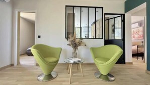 Ein modernes Wohnzimmer mit zwei grünen Sesseln, einem kleinen Tisch mit einem Buch und einer Vase mit Trockenblumen.