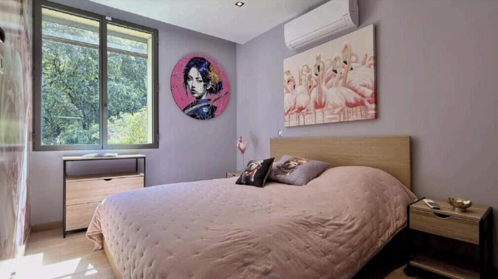 A bedroom with a bed, a desk, a chair, a window, and artwork on the walls.