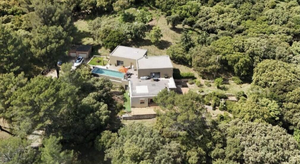 A house surrounded by dense trees, with a swimming pool and a garage.