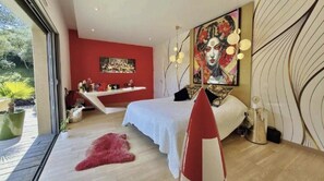 A modern bedroom with a bed, a red accent wall, a large painting, and a view of greenery outside. - Exceptional contemporary villa with infinity pool - Pont du Gard (Remoulins)