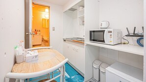 Een compacte keuken met een magnetron, een spoelbak en een klein tafeltje met een stoel.