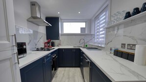 Una cucina moderna con mobili blu scuro, un piano di lavoro bianco, un piano cottura integrato, un forno a microonde e una finestra sopra il lavello.