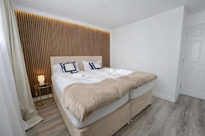 Moderni hotellihuone, jossa on suuri sänky, yöpöytä ja seinäpaneelista tehty koristeellinen seinä.