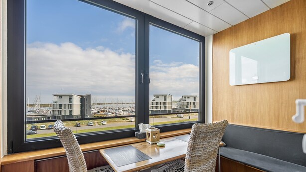 A room with a large window, a wooden desk, two wicker chairs, a bench, and a wall-mounted mirror.