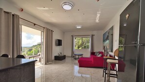 Un vaste espace de vie comprenant un canapé rouge, une table à manger, un coin cuisine avec un réfrigérateur et un balcon offrant une vue agréable.