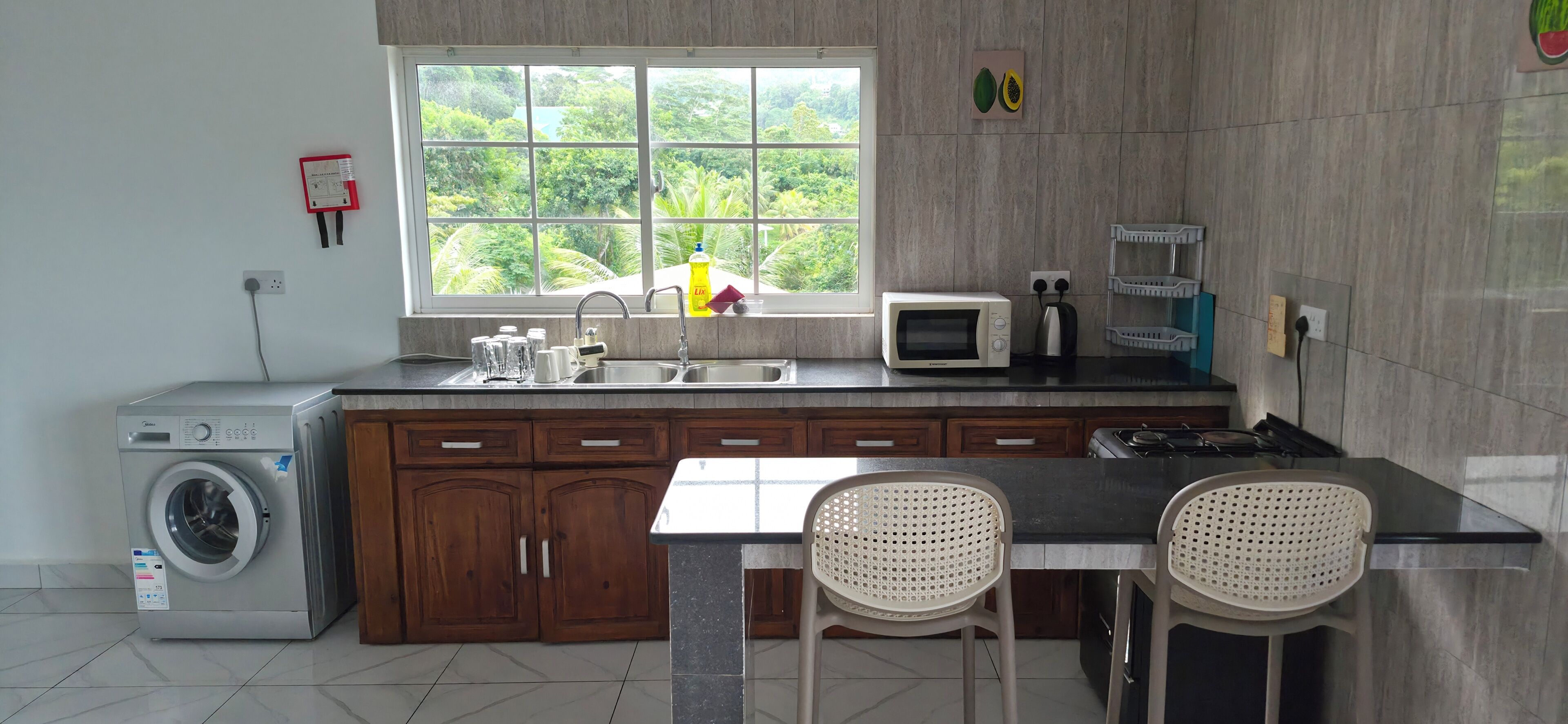 A kitchen with a washing machine, a microwave, a sink, and two chairs.