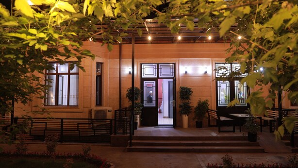 A building with a covered entrance, potted plants, outdoor seating, and a pathway leading to the entrance. - Karaman Hotel (Tashkent)