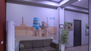A modern lobby with a large mural, a grey sofa, a potted plant, and a door. - Karaman Hotel (Tashkent)