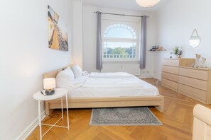 Ein modernes Schlafzimmer mit Bett, Nachttisch, Kommode und einem großen Fenster mit Vorhängen.