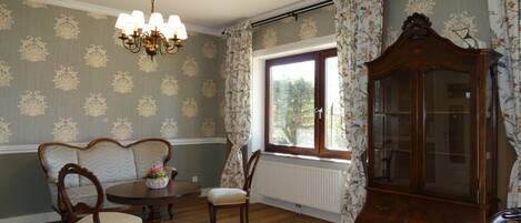 A room with a dining table, chairs, a chandelier, a cabinet, and a window with curtains.