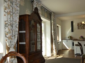 Ein Zimmer mit einem Holzkasten, einem Stuhl, einem Tisch mit einer Blumenkorb und einer Wand mit einer Leuchte.