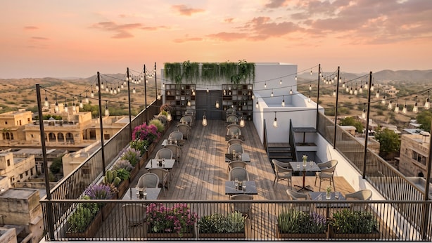 A rooftop terrace with tables and chairs, a garden wall with plants, and a cityscape view. - Eco Boutique Satva Udaipur - Vegetarian with all Options (Udaipur)