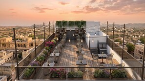 A rooftop terrace with tables and chairs, a garden wall with plants, and a cityscape view. - Eco Boutique Satva Udaipur - Kitchen with No-Onion No-Garlic (Udaipur)