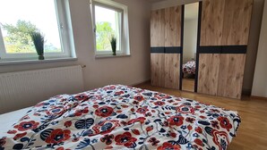 Une chambre à coucher avec un lit, deux fenêtres, un radiateur et une armoire en bois.