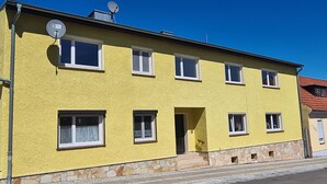 Un bâtiment jaune avec de nombreuses fenêtres, une porte et une antenne parabolique.