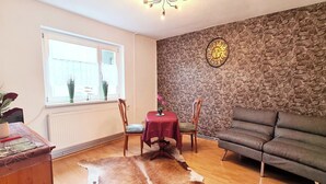 Un salon avec un mur en pierre, un canapé, une table à manger avec des chaises et un tapis en peau de vache.