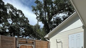 A covered outdoor area with a wooden gate, a white door, and a trash bin. - Sweet home (Brandon)