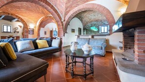 A cozy living area with a brick fireplace, a sofa with cushions, and a table with decorative items. - Casale Le Rondini with a swimming pool and private garden (LUCIGNANO)