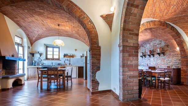 A spacious kitchen with brick arches, a dining area with wooden chairs, and a stone wall with shelves. - Casale Le Rondini with a swimming pool and private garden (LUCIGNANO)