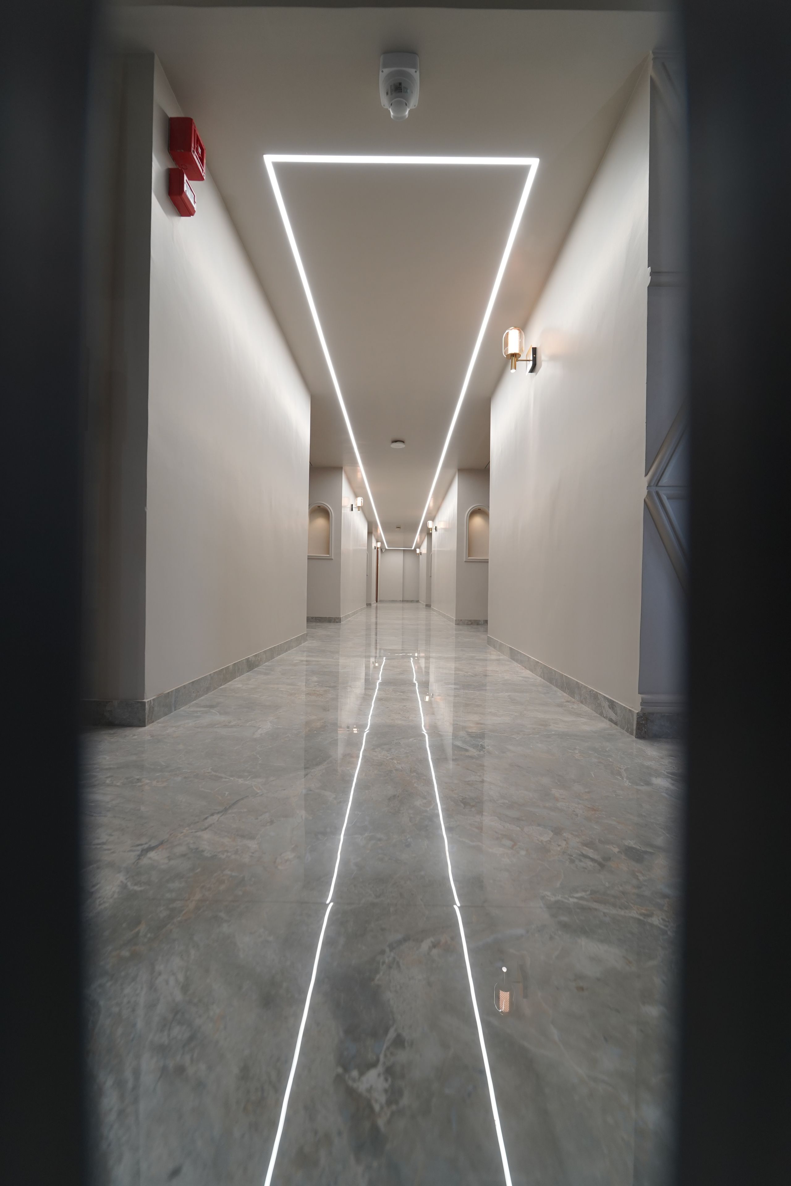 Un pasillo moderno y bien iluminado con una lámpara de techo de diseño geométrico, que conduce a una puerta al final.