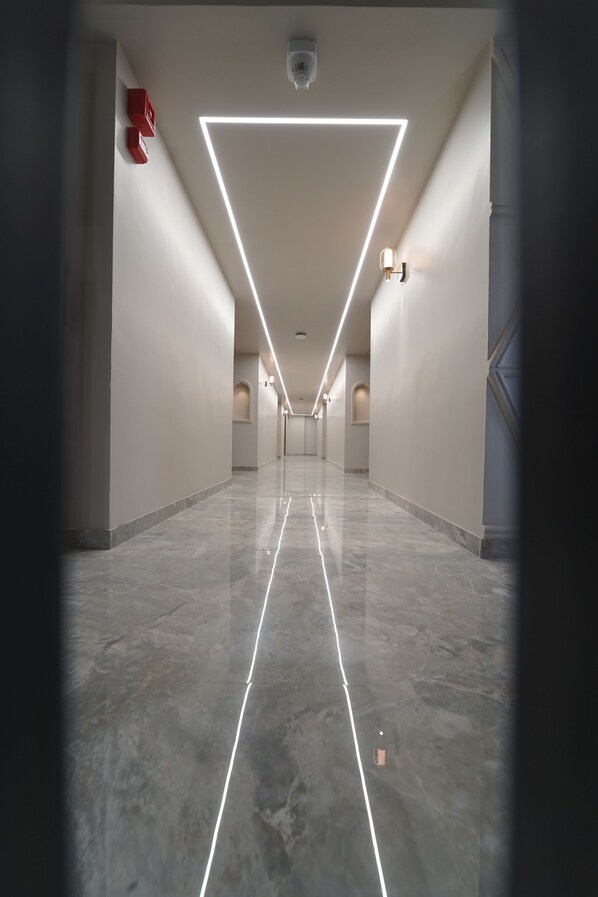A modern, well-lit corridor with a geometric light fixture on the ceiling, leading to a door at the end. - Hotel Repose (Vadodara)
