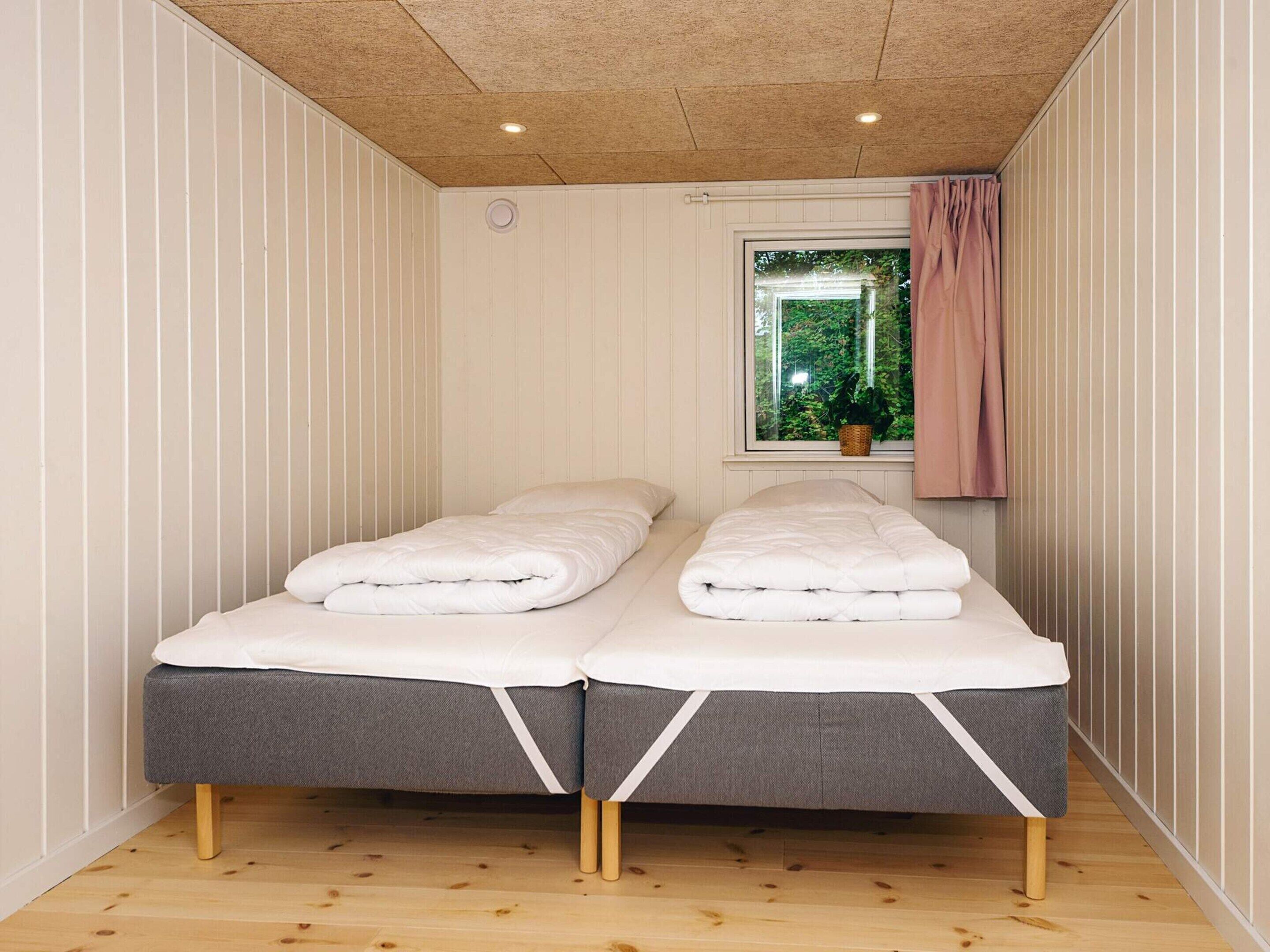 Une chambre avec deux lits simples, une fenêtre donnant sur un espace verdoyant et un plancher en bois.