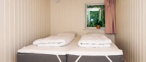 Une chambre avec deux lits simples, une fenêtre donnant sur un espace verdoyant et un plancher en bois.