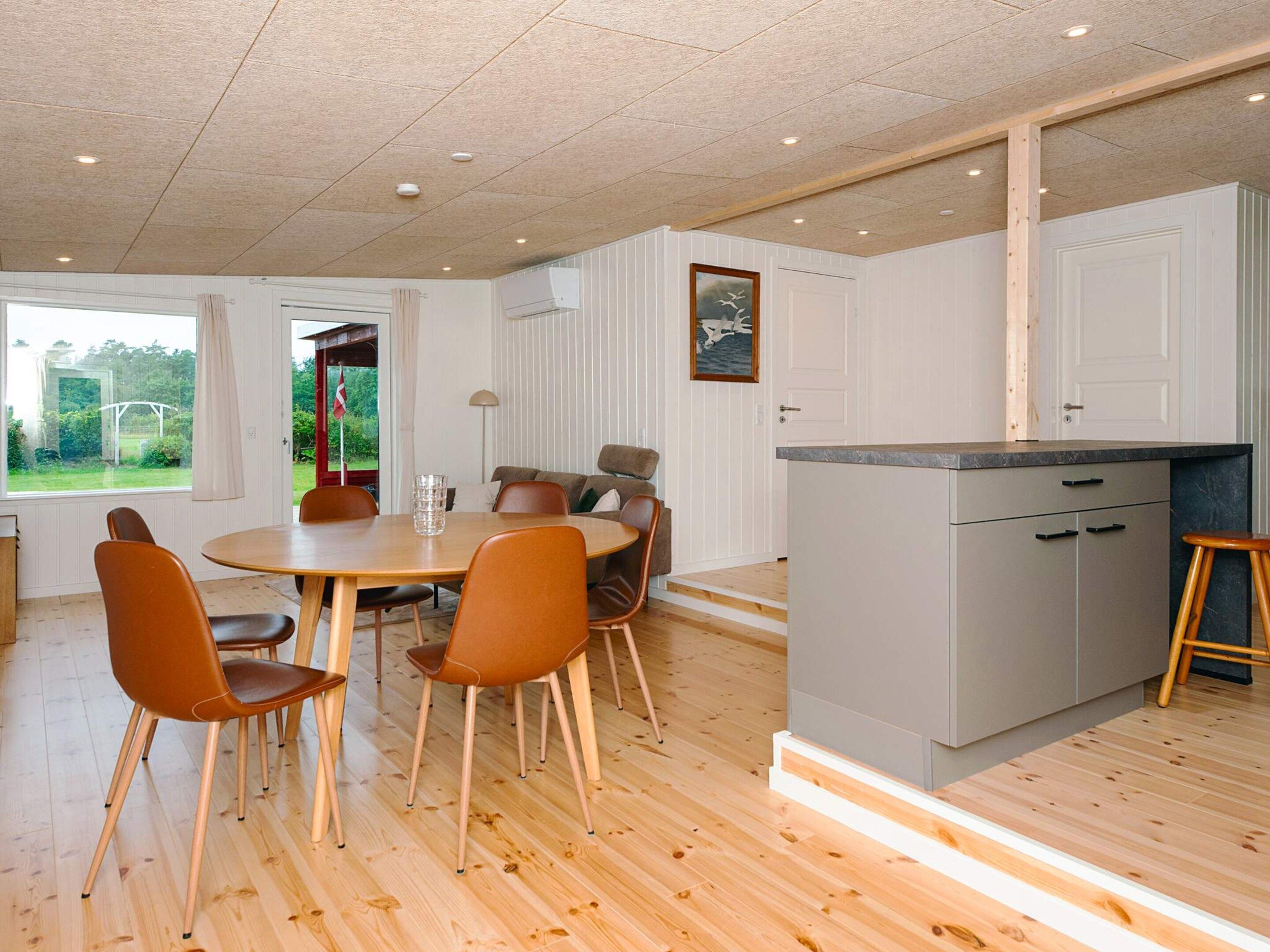 A modern kitchen with a central island, wooden flooring, and a dining area with chairs and a table.