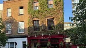 En byggnad med murgrönebeklädda väggar och ett rött markis med texten ”The Atlas”.