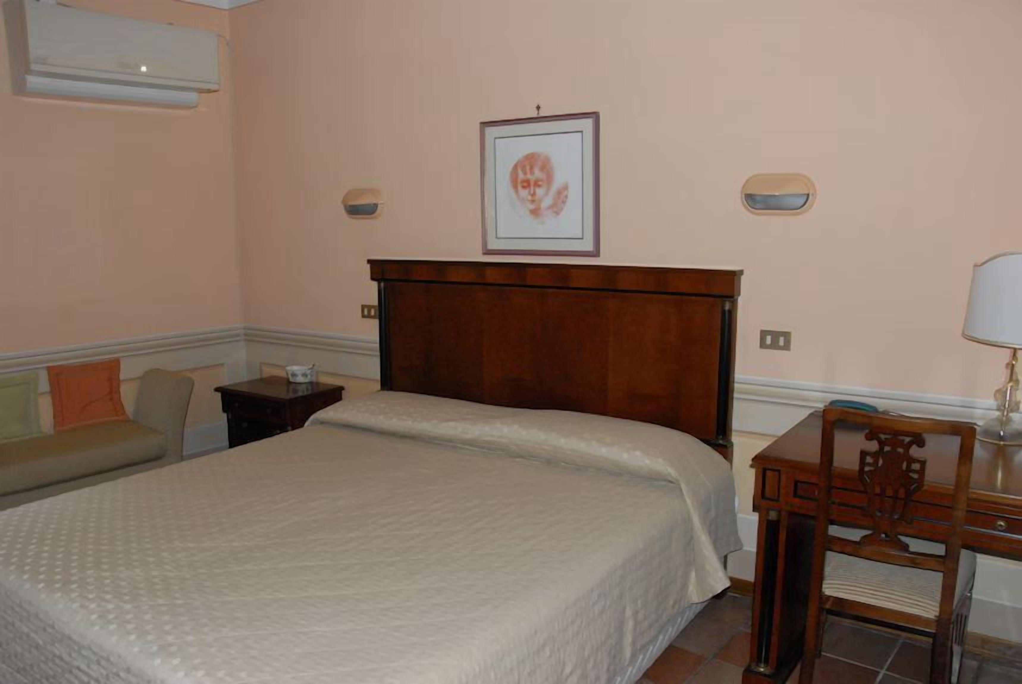 A bedroom with a bed, a nightstand, a chair, a desk, and a wall-mounted picture.