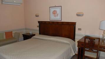 A bedroom with a bed, a nightstand, a chair, a desk, and a wall-mounted picture.