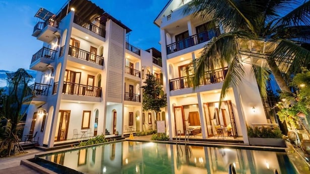 A multi-story hotel with balconies, a swimming pool, and palm trees. - Ony Retreat Villas (Da Nang)
