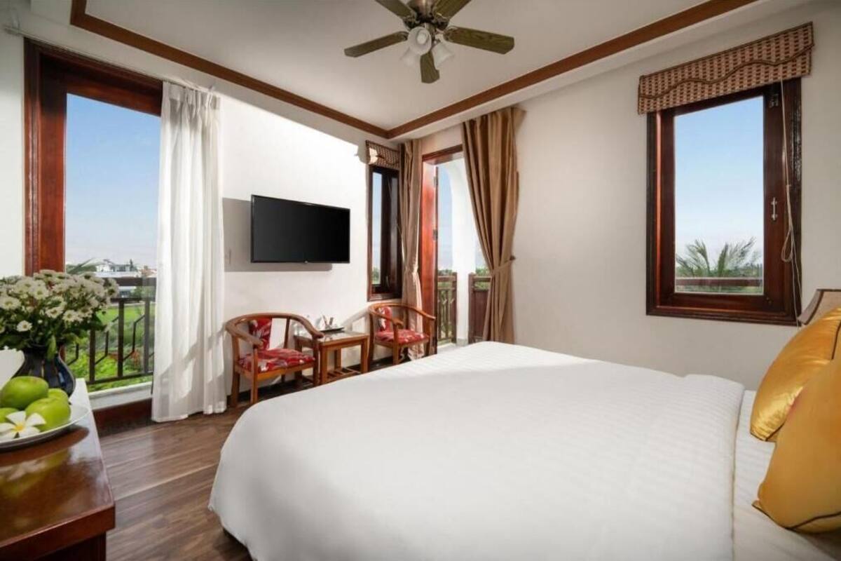 Een hotelkamer met een bed, een televisie, een balkon met een tafel en stoelen, en een plafondventilator.