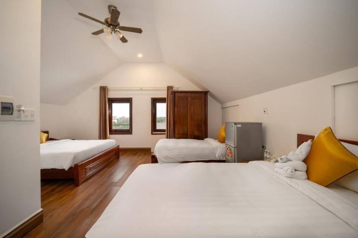 Een kamer met twee bedden, een plafondventilator, een koelkast en een raam met gordijnen.