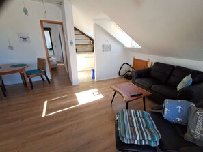 Een woonkamer met een houten vloer, een zwarte leren bank, een gestreept kussen, een houten salontafel en een kleine tafel met stoelen.