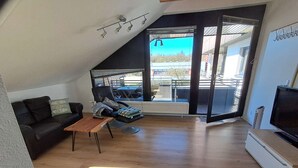 Un soggiorno moderno con un divano in pelle nera, un tavolino in legno, una televisione e un'ampia porta scorrevole in vetro che si apre su uno spazio esterno.