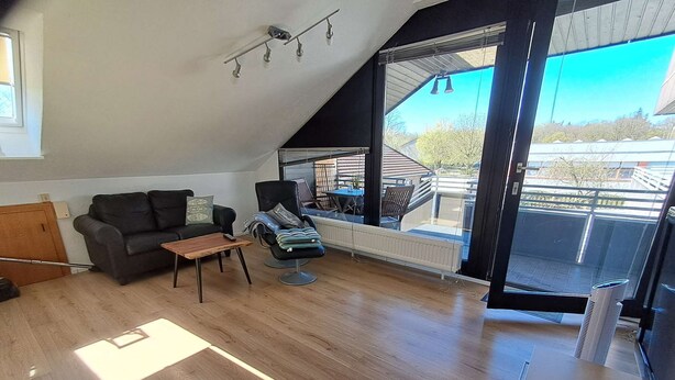 Una camera in stile loft con soffitto a falde, un divano in pelle nera, un tavolino in legno e vista esterna attraverso ampie finestre.