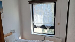 Una camera da letto con un letto, una finestra con tenda, un termosifone e una lampada a parete.