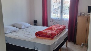 Un dormitorio con cama, ventana con cortinas, mesita de noche y armario.