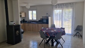 Un comedor con mesa y sillas, una cocina con estufa y alacenas, y un ventanal con cortinas.