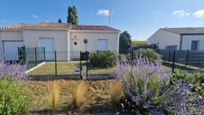 Un edificio residencial con techo de tejas, un jardín cercado con lavanda y un cielo azul despejado.
