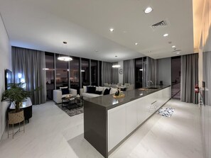 Une cuisine moderne avec un îlot central, un coin repas avec un canapé et un salon équipé d’un téléviseur.