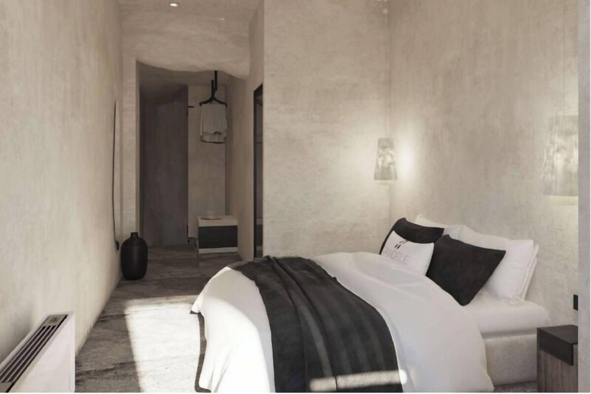 Une chambre à coucher moderne, avec un lit, des tables de chevet, un luminaire suspendu et une vue sur le couloir.
