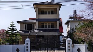 Un edificio residencial de varios pisos con entrada protegida por una reja, un tanque de agua en el techo y un pequeño balcón en el piso superior.