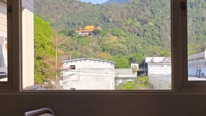 Una habitación con vistas a la montaña, un edificio tradicional y una pequeña mesa con un jarrón de flores.