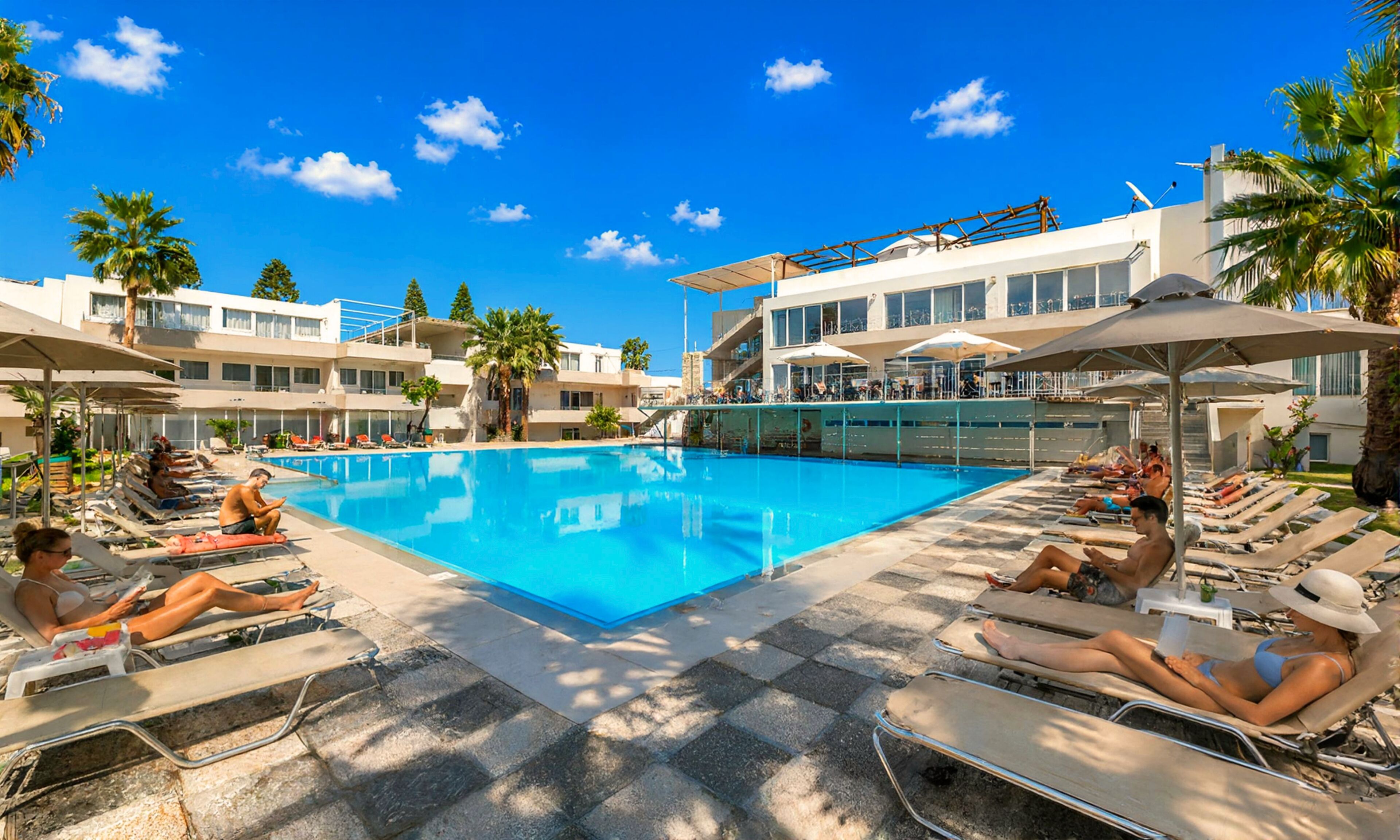 A pool area with lounge chairs, umbrellas, and a building with balconies.