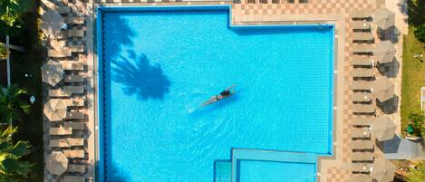 Ein großer, rechteckiger Swimmingpool mit einer darin schwimmenden Person, umgeben von Liegestühlen und Sonnenschirmen.