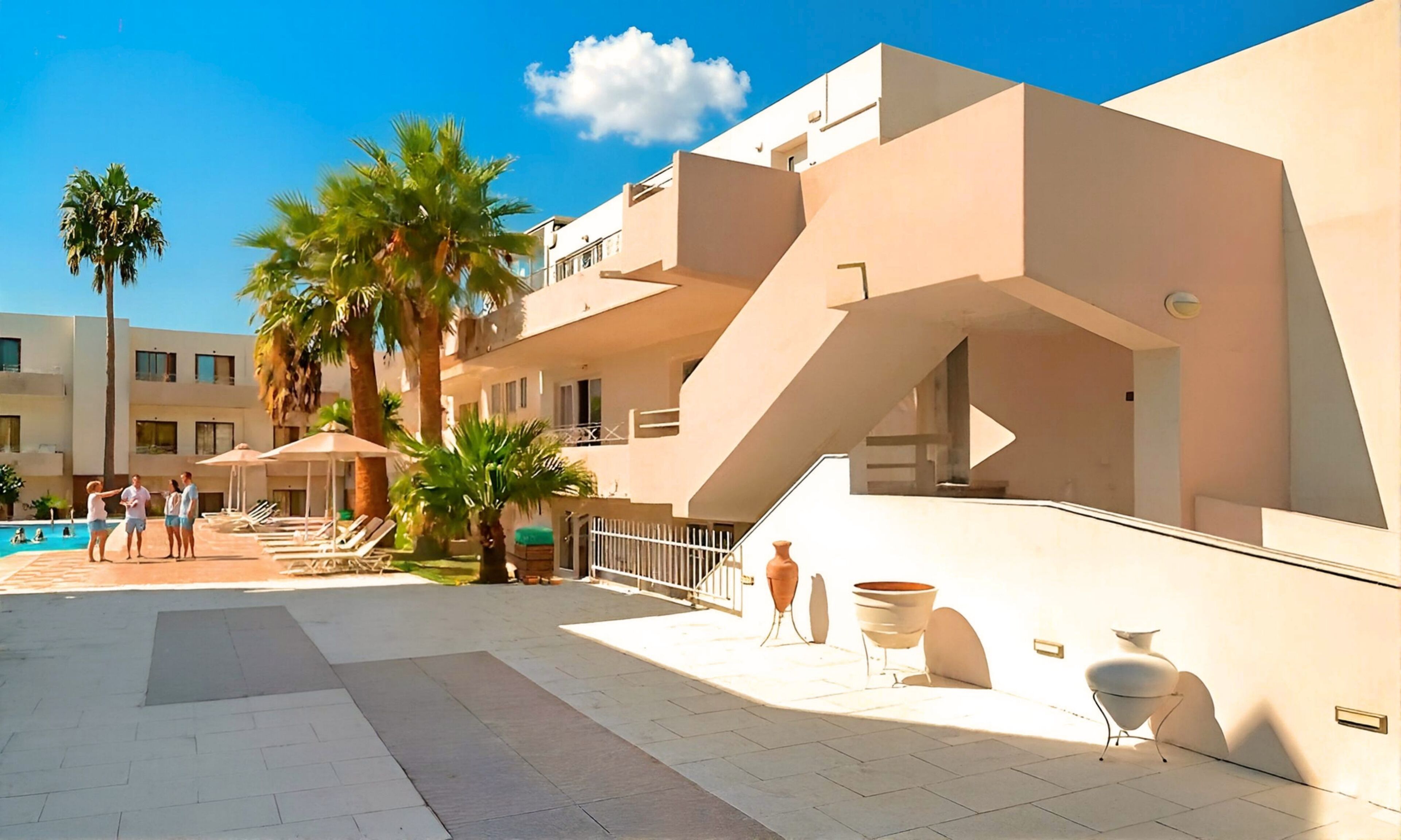 A modern building with a pool area, palm trees, and outdoor seating.